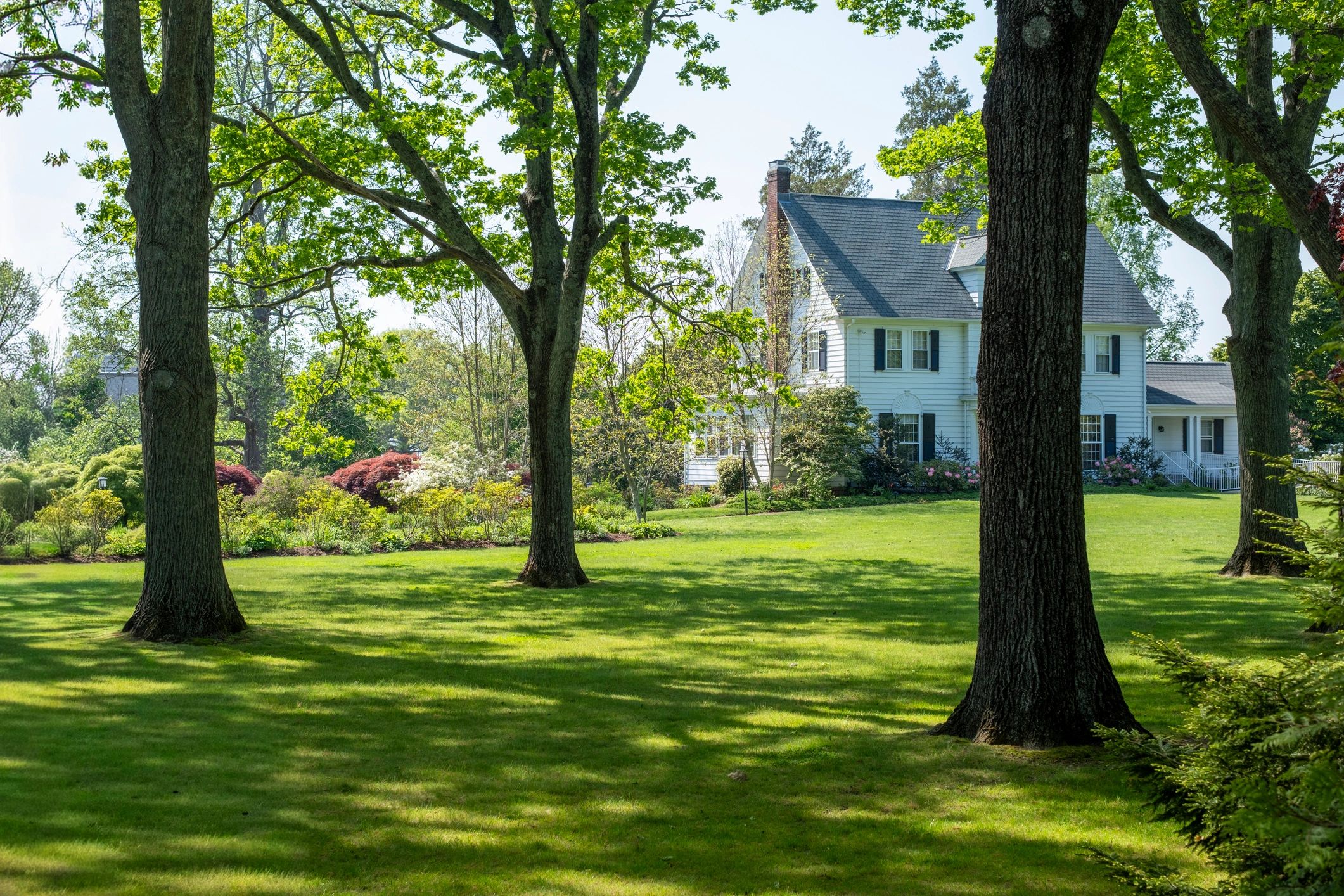 Large white country house with spacious green lawn and trees